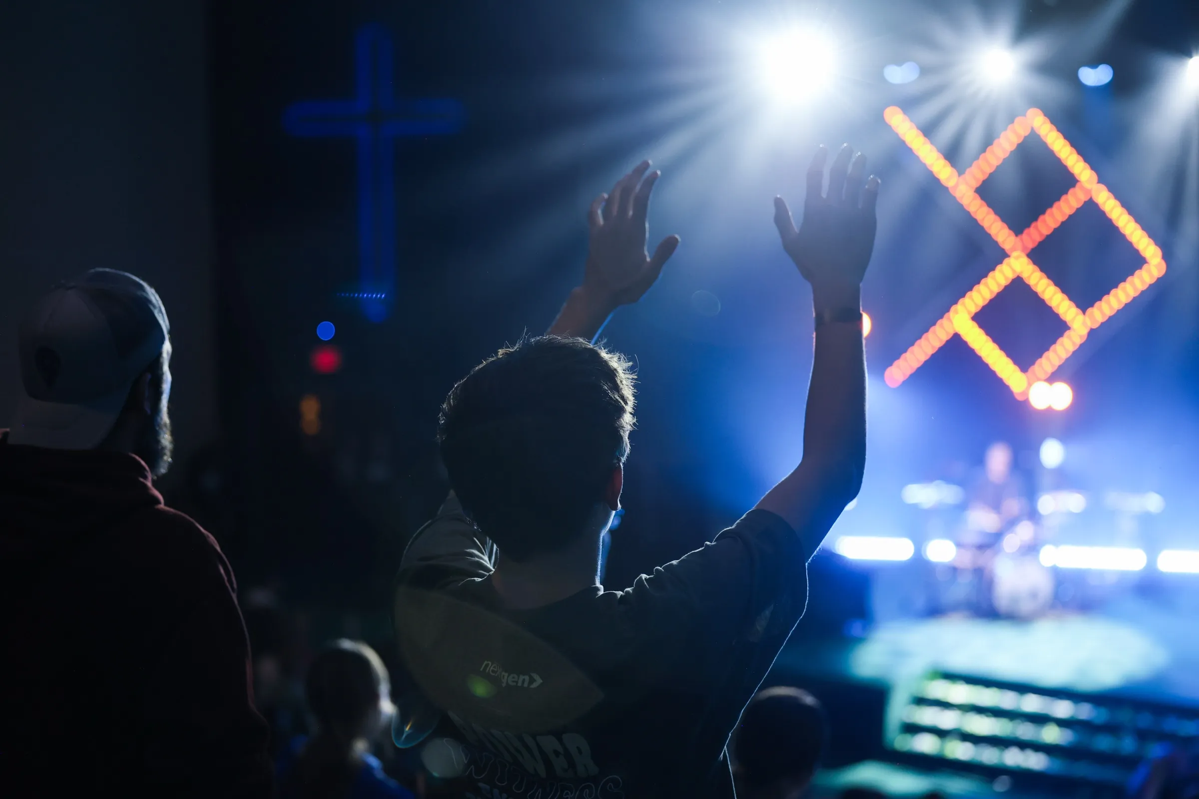 Students with raised hands beneath a lit cross
